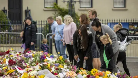 PA/Liam McBurney Members of the public look at flowers and wreaths left in remembrance to Queen Elizabeth II at Hillsborough Castle in Northern Ireland. Picture date: Monday