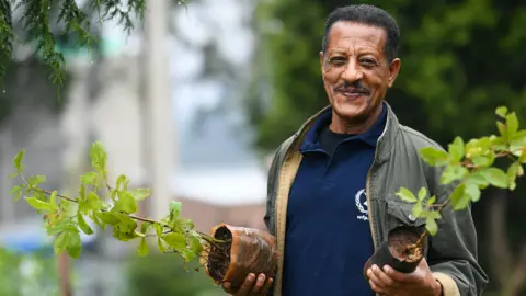 AFP An Ethiopian man poses holding tree seedlings during a national tree-planting drive in the capital Addis Ababa - 28 July 2019