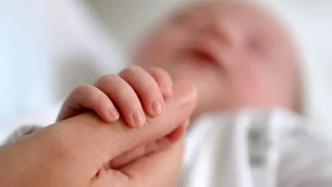 PA Media A newborn baby grasping the thumb of her mother,