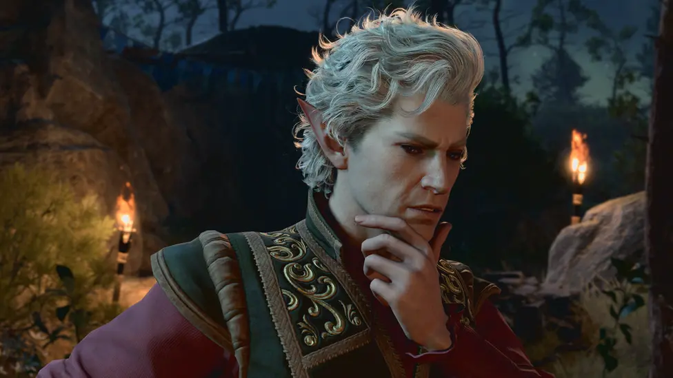 Larian Studios A man with white hair, pointed ears and unusually pale skin puts his hand to his chin, apparently deep in thought. He wears a high-necked, elaborate green jacket, with golden patterning on the shoulders. The Medieval garment has deep purple sleeves. He's in what appears to be a forested area. It's night-time, and two flaming torches attached to rocks in the background illuminate the scene