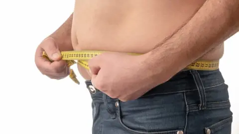 Getty Images Barechested man measures waist with measuring tape