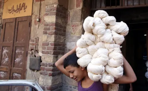 EPA Moustafa, 15, carries white yarn rolls at Salama"s tannery in Cairo, Egypt, 07 November 2017. Salama started working when he was seven years old during the reign of King Farouk over Egypt because, according to him, the police used to arrest unemployed males of all ages. Now, after almost 70 years, Salama"s tannery is the only one left in the old part of Cairo. The yarn produced is used for shoe laces, mattresses upholstery, ballet dance outfits,
