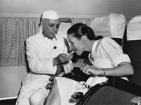 BBC Mr Nehru lights a cigarette for the wife of a British diplomat while on board the first BOAC or round-the-world flight in India.