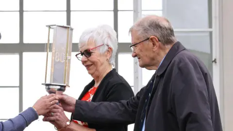 Commonwealth War Graves Commission Frances Dodson and Peter Clare handing the torch of commemoration to an air cadet at Runnymede Air Forces Memorial