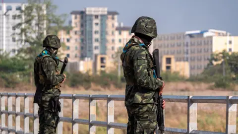 Jonathan Head/BBC Tall buildings in Myanmar's Myawaddy seen from Thailand's border, where armed guards stand on a bridge
