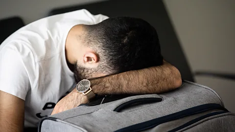 Getty Images A man sleeping on his luggage at the airport (Credit: Getty Images)